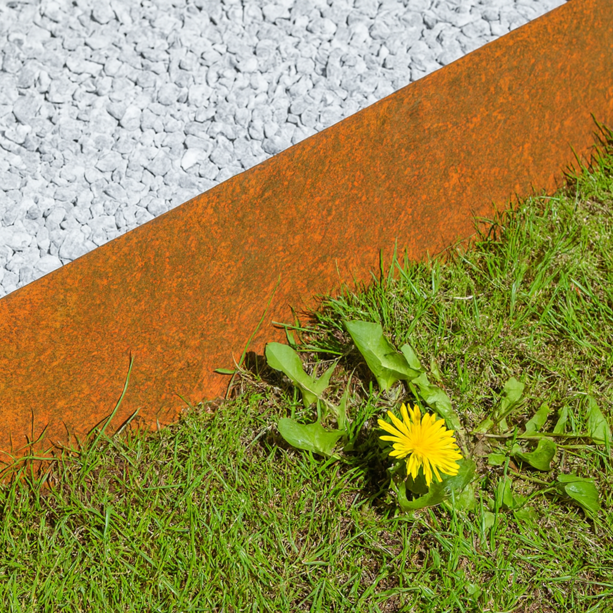 Cortenstahl Beeteinfassung trennt weißen Zierkies von grünem Rasen – langlebige Rasenkante aus Edelrost für moderne Gartengestaltung.